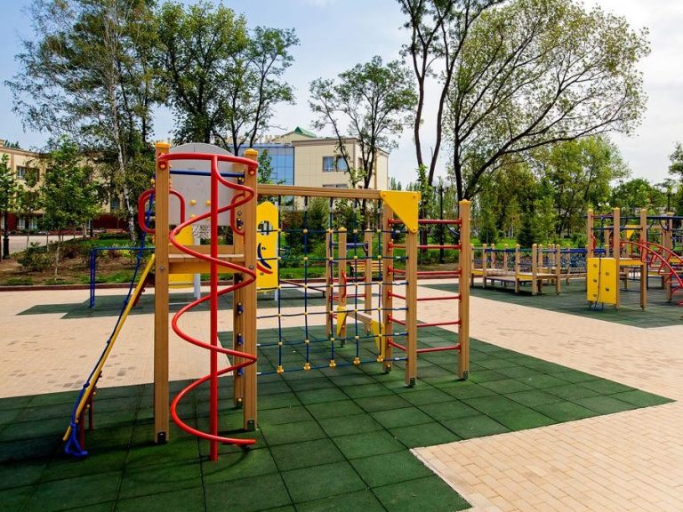 Großer Kinderspielplatz mit Holzspielgeräten und grasgrünen Fallschutzböden