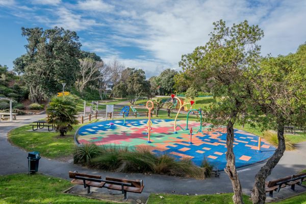 ein öffentlicher Spielplatz mit runder Fallschutzfläche in vielen bunten Farben, umgeben von grüner Natur